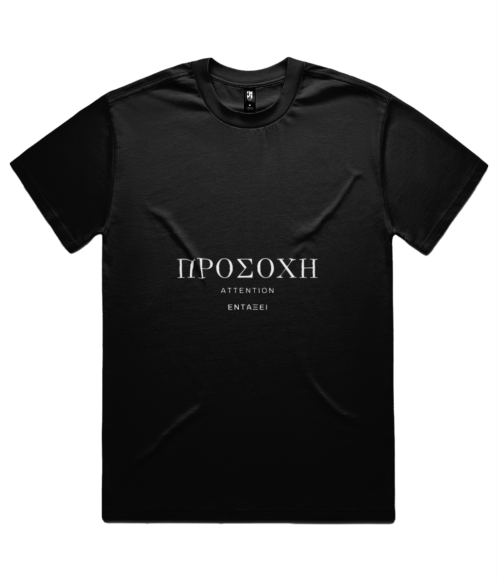 Black ΠΡΟΣΟΧΗ Tee shown flat on white, front print: ΠΡΟΣΟΧΗ in Didot capitals with ATTENTION beneath and the ΕΝΤΑΞΕΙ wordmark below.