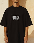 Model wearing the black Thesis Tee against a sunlit cream plaster wall, MARCUS WROTE IN GREEK printed across the chest in bold sans capitals.