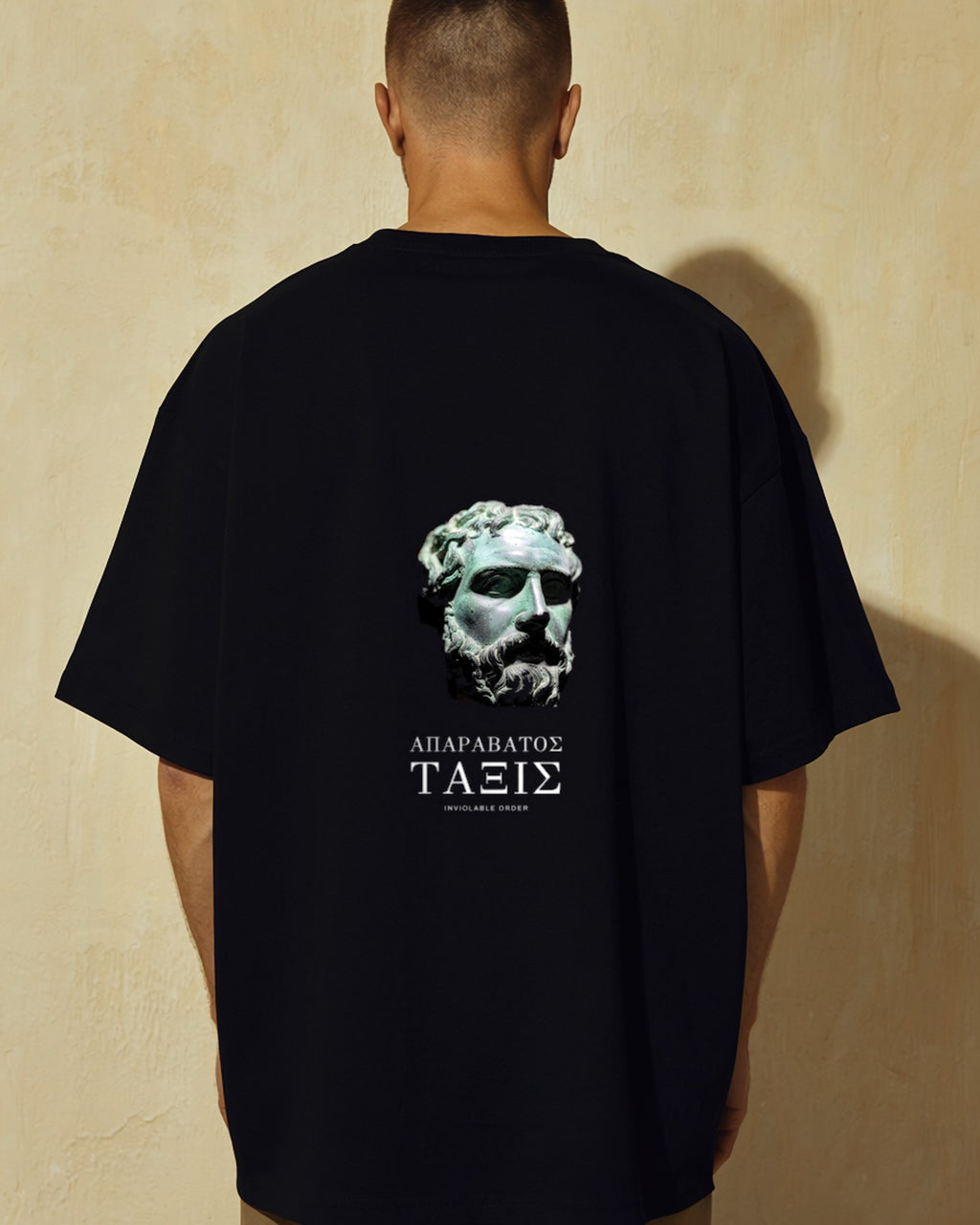 Model seen from behind wearing the black Salvage Tee, corroded bronze head printed across the back