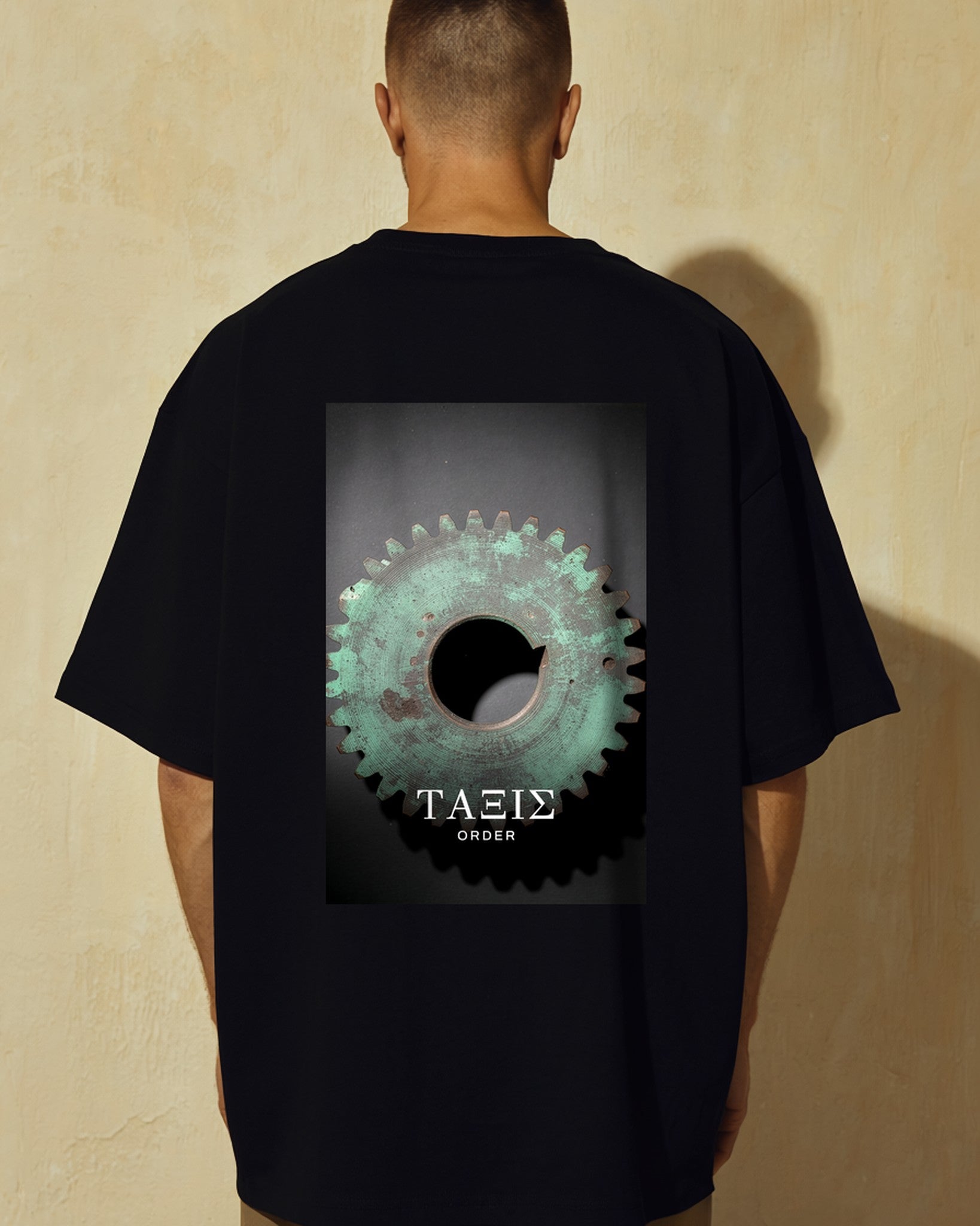 Model seen from behind wearing the black Mechanism Tee, ancient bronze gearwork printed across the back