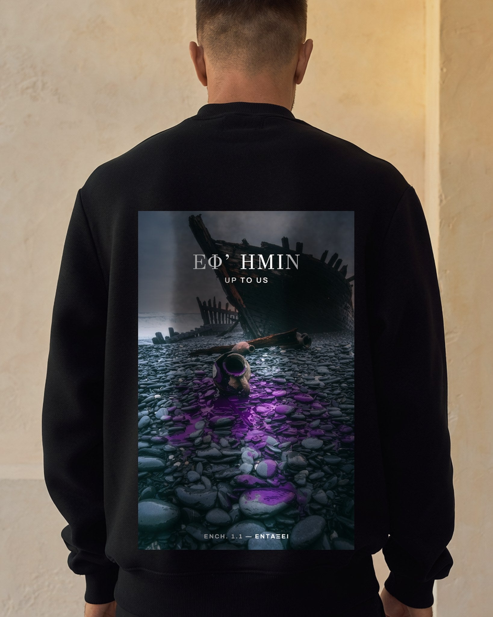 Model seen from behind wearing the black Citium Crew sweatshirt against a sunlit cream plaster wall, the shipwreck and spilled purple dye printed across the back.
