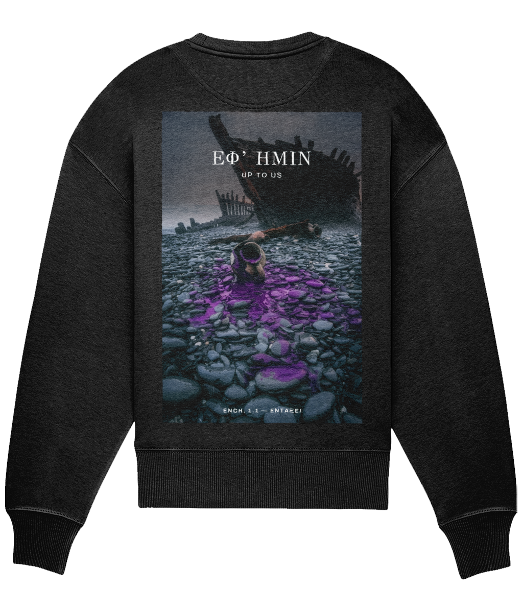 Black ΕΦ’ ΗΜΙΝ oversized sweatshirt shown flat on white from the back, full back print: a storm beach with a wrecked hull and purple dye across the stones, ΕΦ’ ΗΜΙΝ above with UP TO US beneath and ENCH. 1.1 — ΕΝΤΑΞΕΙ at the base.